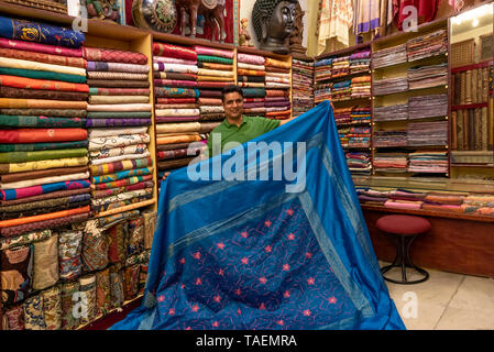 Horizontale Porträt eines Ladenbesitzers zeigt eine Seiden-sari in seinem Geschäft in Indien. Stockfoto