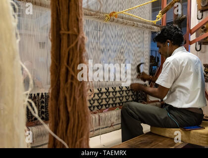 Horizontale Ansicht von einem Mann hören auf sein iphone mit einem altmodischen senkrechten Webstuhl in Indien. Stockfoto