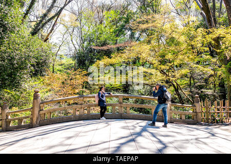 Tokio, Japan - 3. April 2019: Meiji-Schrein mit grünem Baumwald im Frühling und Touristen, die auf einer Brücke im Park fotografieren Stockfoto