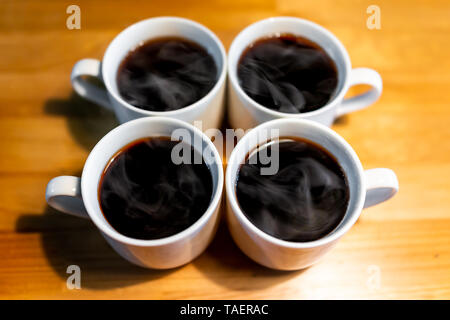 Nahaufnahme von vier Tassen Kaffee oder puerh schwarzer Tee mit heißem Dampf auf hölzernen Tisch Stockfoto