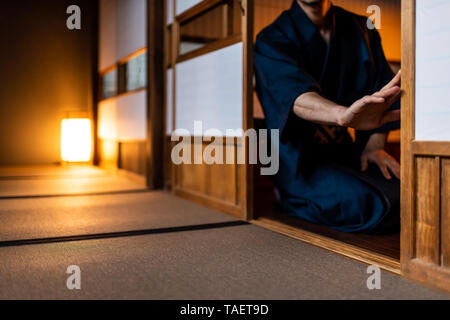 Traditionelle japanische Haus oder Ryokan mit Mann im Kimono Eröffnung shoji Schiebetüren Papier Türen sitzen auf Tatami Matten Boden Stockfoto