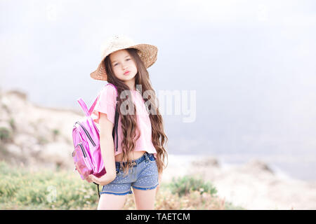 Stilvolle Baby Mädchen mit trendigen Sommer Kleidung und rosa Rucksack im Freien. Mit Blick auf die Kamera. Stockfoto