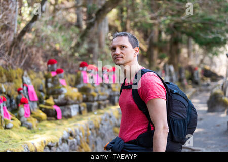 Nikko, Japan und junge glücklich Mann an Jizo Statuen in den berühmten Kanmangafuchi Abgrund in der Präfektur Tochigi in Japan im Frühjahr auf der Suche Stockfoto