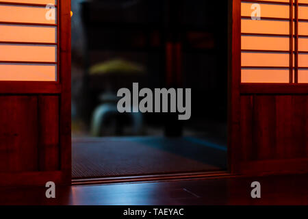 Traditionelle japanische Haus oder Ryokan Restaurant in dunklen Abend Nacht Hintergrund von Shoji Papier Tür Schiebetür mit Stein Laterne im Garten Stockfoto