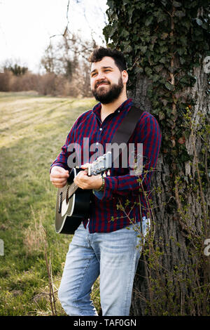 Mann Gitarre zu spielen, ein Baum auf der Wiese Stockfoto