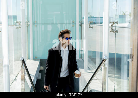 Portrait von Geschäftsmann mit Sonnenbrille, Kaffee trinken gehen und Gepäck auf Treppen Stockfoto