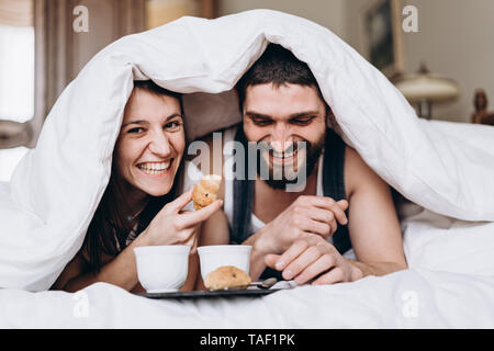 Glückliches Paar essen Croissants in Ihrem Bett am Morgen Stockfoto