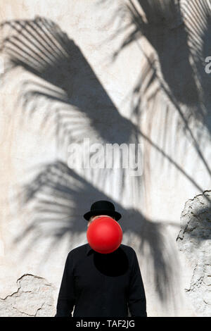 Marokko, Essaouira, Mann mit einem Bowler Hut mit roten Ballon vor seinem Gesicht an der Wand Stockfoto