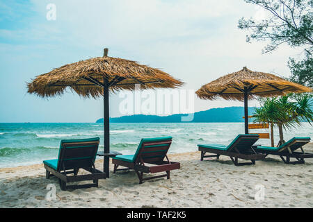 Strand ruhige Szene mit Sonnenliegen und Sonnenschirme Stroh unter Kokospalmen in der Nähe der Karibik. Tropisches Paradies mit Chaiselounges auf weißem Sand, Bea Stockfoto