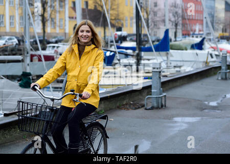 Dänemark, Kopenhagen, glückliche Frau Reiten Fahrrad am Hafen der Stadt im regnerischen Wetter Stockfoto