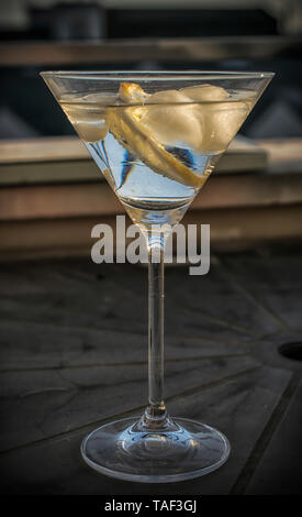 Ein großer Cocktail Glas mit transparenten Getränk, Eis und Zitrone auf einem Tisch Stockfoto