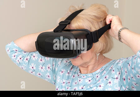 Portsmouth, UK, Mai 2019. Ältere Frau ziehen über den Kopf ein paar virtuelle Realität Schutzbrille Stockfoto