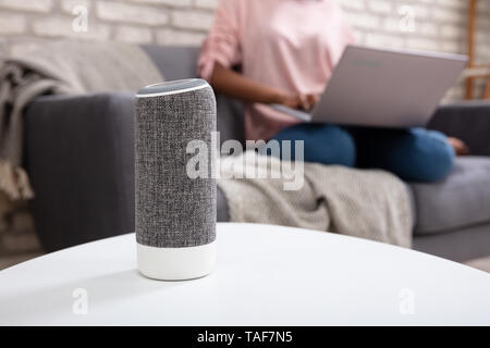 Frau mit Laptop über Voice Assistant Lautsprecher zu Hause Stockfoto
