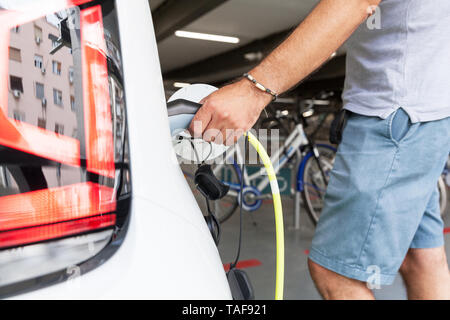 Ein Mann hält in der einen Hand einen elektrischen Plug-in für das Laden von Elektroautos Stockfoto