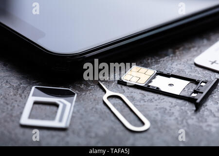 Handy in der Nähe von Nano-SIM-Karte in den Card Adapter mit Eject Pin über konkreten Hintergrund Stockfoto