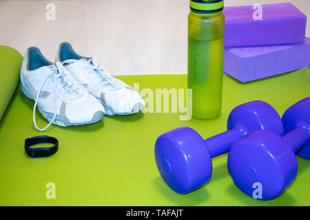 Fintes Kurzhanteln, Turnschuhe, eine Flasche Wasser, fitness Armband und lila Würfel auf der grünen Matte, Sport Konzept, horizontale Foto Stockfoto