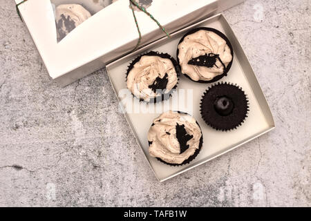 Schöne Schokolade Sahne cupcakes in ein weißes Kästchen mit einem Seil an einem konkreten Hintergrund gebunden Stockfoto