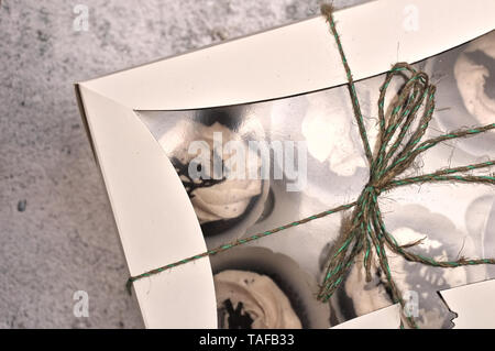 Schöne Schokolade Sahne cupcakes in ein weißes Kästchen mit einem Seil an einem konkreten Hintergrund gebunden Stockfoto