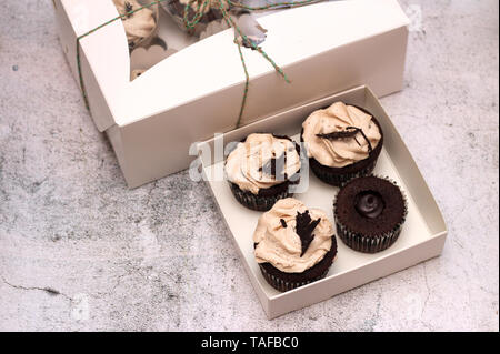 Schöne Schokolade Sahne cupcakes in ein weißes Kästchen mit einem Seil an einem konkreten Hintergrund gebunden Stockfoto