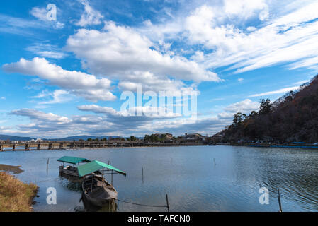 Boot an Hozu-gawa Fluss und Togetsu-kyo Brücke mit bunten Wald Berg Hintergrund in Arashiyama, Kyoto, Japan. Arashiyama ist ein National Desig Stockfoto