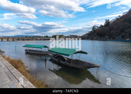 Boot an Hozu-gawa Fluss und Togetsu-kyo Brücke mit bunten Wald Berg Hintergrund in Arashiyama, Kyoto, Japan. Arashiyama ist ein National Desig Stockfoto