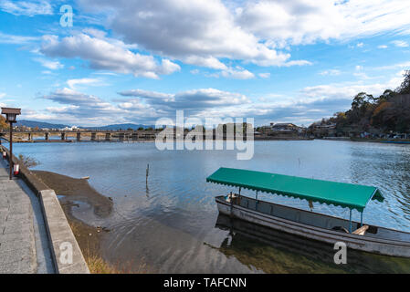 Boot an Hozu-gawa Fluss und Togetsu-kyo Brücke mit bunten Wald Berg Hintergrund in Arashiyama, Kyoto, Japan. Arashiyama ist ein National Desig Stockfoto