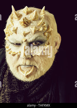 Monster mit gerunzelter Stirn Gesicht und weißen Augen. Mann mit Drachen Haut und Bart. Alien oder reptilian Make-up mit Dornen und Warzen. Daemon Kopf auf Schwarz backgr Stockfoto