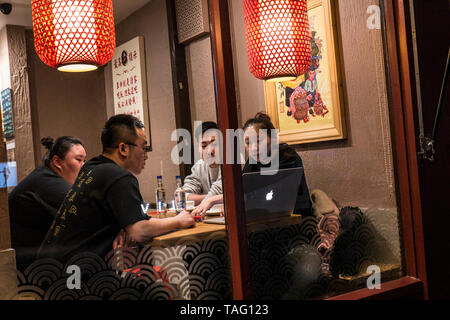 Orientalische Gruppe von vier zwischen 25 und 35 Jahren in ein Chinatown chinesische Restaurant an einem Tisch, Überprüfung der Bildschirm Informationen über ein Apple MacBook Computer Soho Chinatown West End London UK sitzen Stockfoto