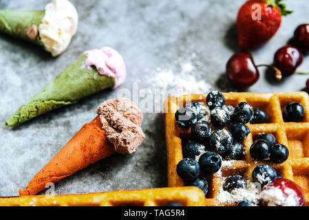 Süße Waffeln mit leckeren roten Früchte voller gesunder Vitamine mit etwas Eis mit Waffeln, über blaue Stein Hintergrund mit Kopie Platz für Text. Stockfoto