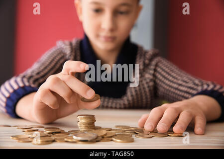 Süße kleine Jungen mit Münzen bei Tisch sitzen. Konzept der Child Support Stockfoto