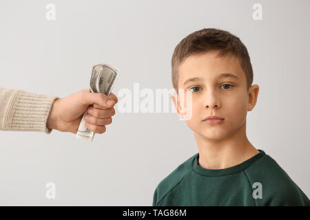 Traurig kleiner Junge und männliche Hand mit Dollar Banknoten auf hellen Hintergrund. Konzept der Child Support Stockfoto