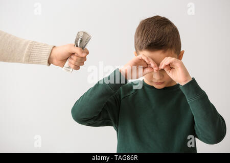 Traurig kleiner Junge und männliche Hand mit Dollar Banknoten auf hellen Hintergrund. Konzept der Child Support Stockfoto