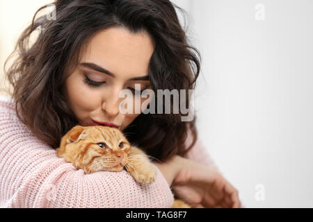 Junge Frau mit niedlichen lustige Katze auf hellen Hintergrund Stockfoto