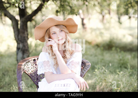 Hübsches blondes junges Mädchen 16-18 Jahre alten trug Hut und eleganten weißen Kleid im Freien. Sommer. Stockfoto