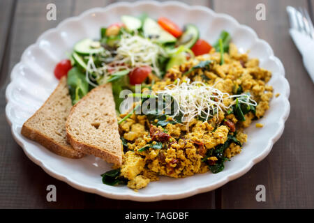 Tofu Rührei mit sonnengetrocknete Tomaten und Spinat und Tomaten und Gurken Salat mit Brot, Stockfoto