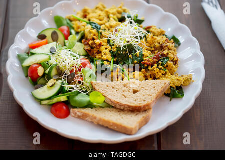 Tofu Rührei mit sonnengetrocknete Tomaten und Spinat und Tomaten und Gurken Salat mit Brot, Stockfoto
