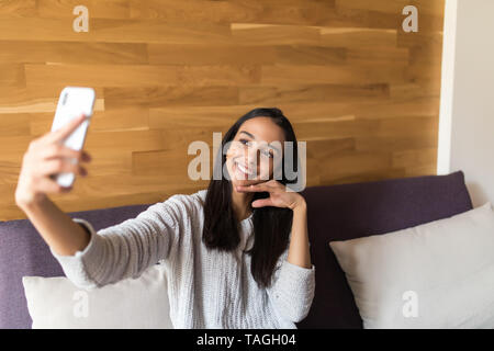 Porträt einer schöne Brünette eine selfie mit Ihrem Smart Phone zu Hause Stockfoto