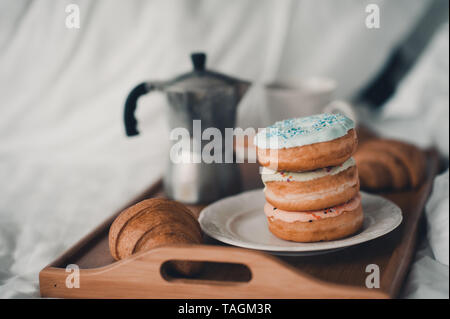 Morgens Kaffee mit glasierten Krapfen und Croissant auf Holz Fach im Bett. Leckeres Frühstück. Selektive konzentrieren. Stockfoto