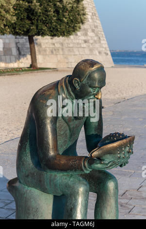 ZADAR, KROATIEN - 10. JULI 2016: Skulptur von einem Mann hält eine Muschel und Blick auf das Meer Stockfoto