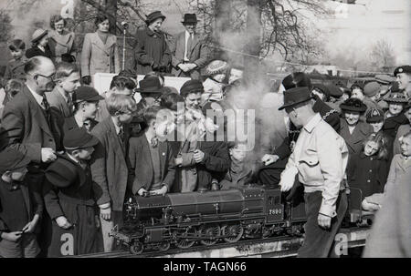 1950, historische, eine Masse von Menschen zu einem Miniatur Dampfzug auf einer Modellbahnanlage suchen, mit einem lokalen possiblly dignitry, der Bürgermeister mit einer Fahrt auf es, England, UK. Diese enge gauage Miniatur-eisenbahn liegt über dem Boden und der Fahrer und Passagiere erhöhte sich rittlings auf die Spur. In dieser ära Modell oder Miniatur Eisenbahnen mit Dampflokomotiven waren eine beliebte Attraktion in Parks und Badeorten. Stockfoto