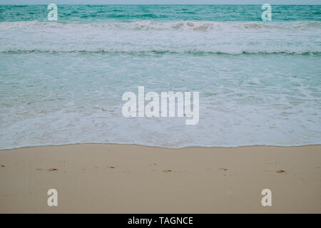 Fußabdrücke auf dem feinen Sand, Meer und Wellen Schaum in den Strand. Selektive konzentrieren. Kopieren Sie Platz. Minimalistisch. Stockfoto