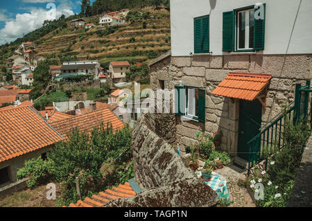 Hausfassade und hügelige Landschaft mit Bäumen und terrassenfelder an Alvoco da Serra. Ein niedliches Dorf auf einem steilen Tal im Osten Portugal festhalten. Stockfoto