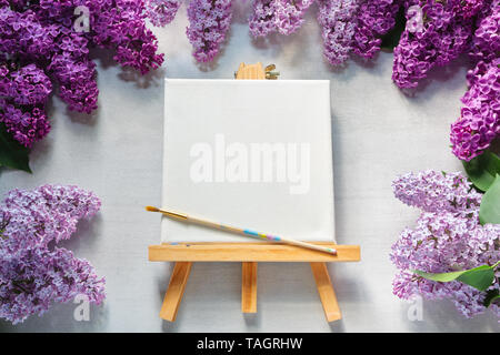 Leere Leinwand auf Staffelei, Pinsel für Malerei und lila Blüten. Stockfoto