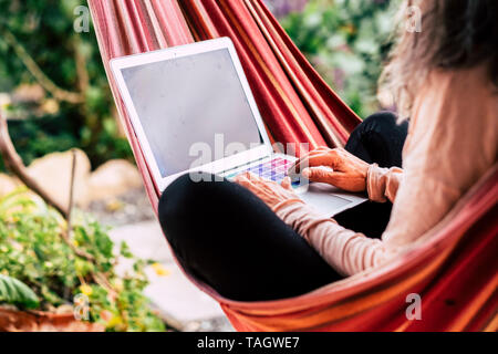 Alte Dame, die Computer Laptop sitzen auf einem farbigen Hängematte - Job und Arbeit überall mit Internet Anschluss WLAN - aktive Leute und Moderne Stockfoto