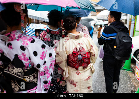 Kyoto, Japan - 9. April 2019: Viele Frauen im Kimono und Sonnenschirme closeup Wandern während der regnerischen Tag auf Higashiyama Street in der Nähe der Kiyomizu-dera Tempel Stockfoto