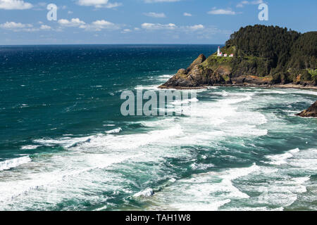 Ein Leuchtturm an der Küste von Oregon sitzt auf schroffen Steilküsten. Unterhalb der Wellen brechen, wie sie in Richtung Strand bewegt. Stockfoto