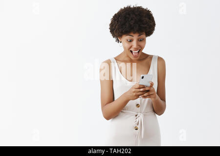 Studio shot von Angeregten charmante dunkelhäutige Frau mit Afro Frisur ja sagen, während beeindruckt und zufrieden, die Nachricht von der Nähe Stockfoto