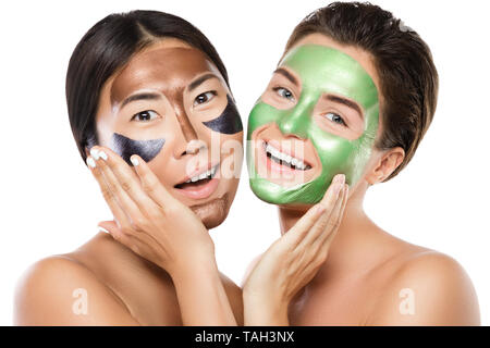 Zwei schöne Mädchen mit bunten Peel-off Maske auf ihren Gesichtern. Auf weissem Hintergrund Stockfoto