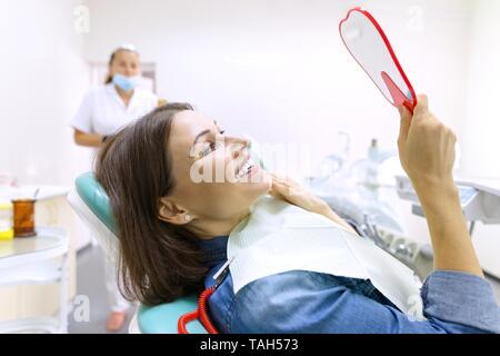 Prozess der zahnmedizinischen Behandlung. Weibliche Patienten mit Blick auf Ihre Zähne im Spiegel während der Sitzung in zahnmedizinischen Stuhl. Gesundheit, Medizin und Zahnmedizin Konzept Stockfoto