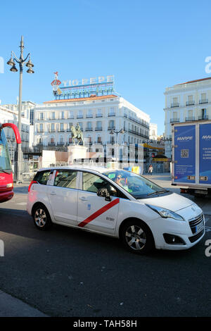 Taxi im Verkehr vor der Puerta del Sol in Madrid, Spanien; iconic Tio Pepe Leuchtreklame und Charles III Statue im Hintergrund. Stockfoto